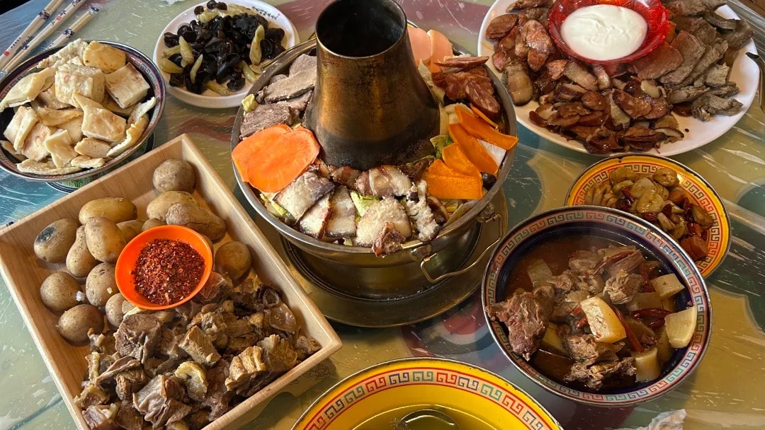 A Tibetan meal spread with a copper hotpot, yak meat dishes and butter tea in brass pots.