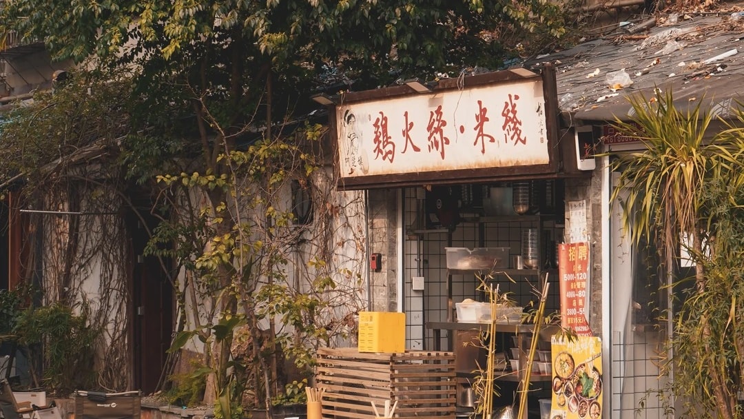 An old Chengdu street with a signboard shopfront, bamboo stools and low tables on the pavement.