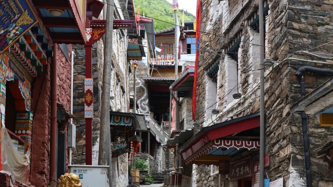 A woman in traditional dress walking a stepped stone lane between old Tibetan buildings in Danba.