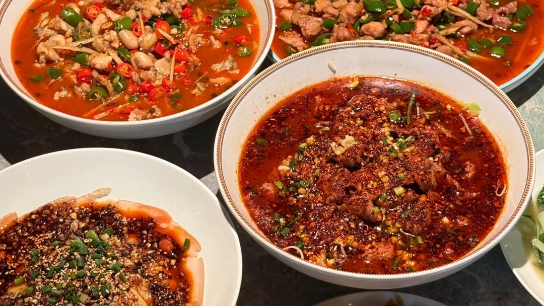 Bowls of classic Sichuan dishes in chili oil arranged on a marble table.