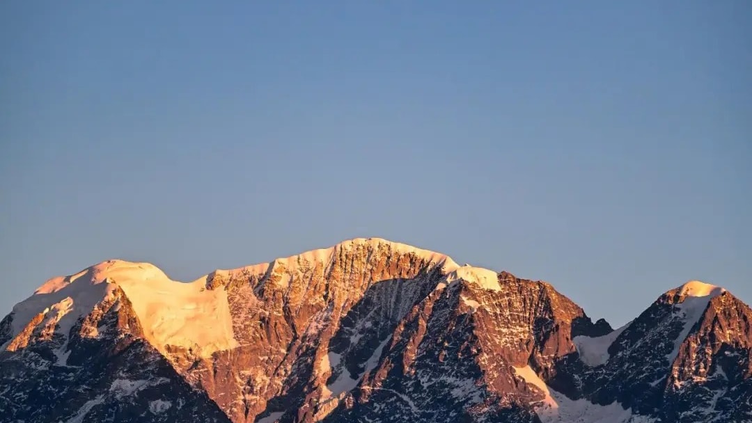 A snow-covered summit ridge catching the first light above dark forested slopes.