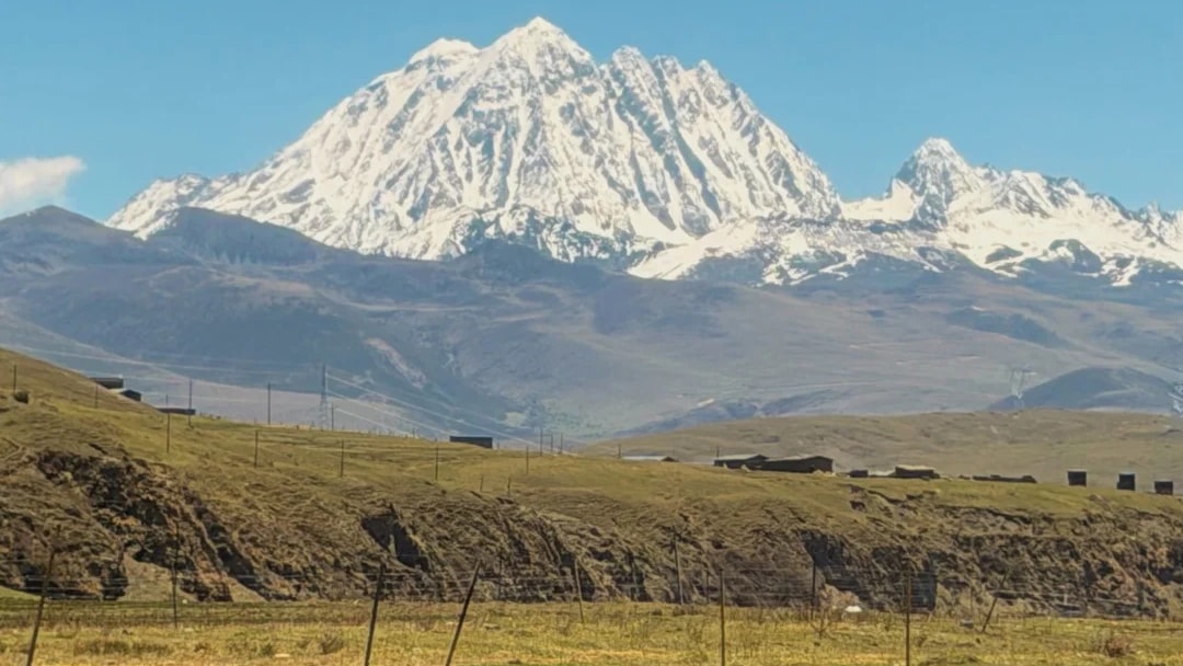 Yaks grazing on open grassland below a jagged snow-capped ridge in western Sichuan.