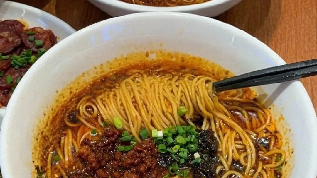 Two bowls of dan dan noodles topped with chili oil, minced pork and spring onion.
