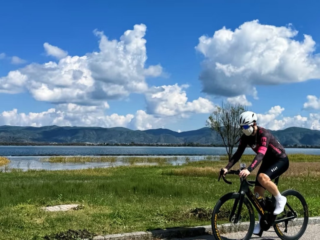 Cyclist on the grassy lakeside greenway with Erhai and distant hills behind
