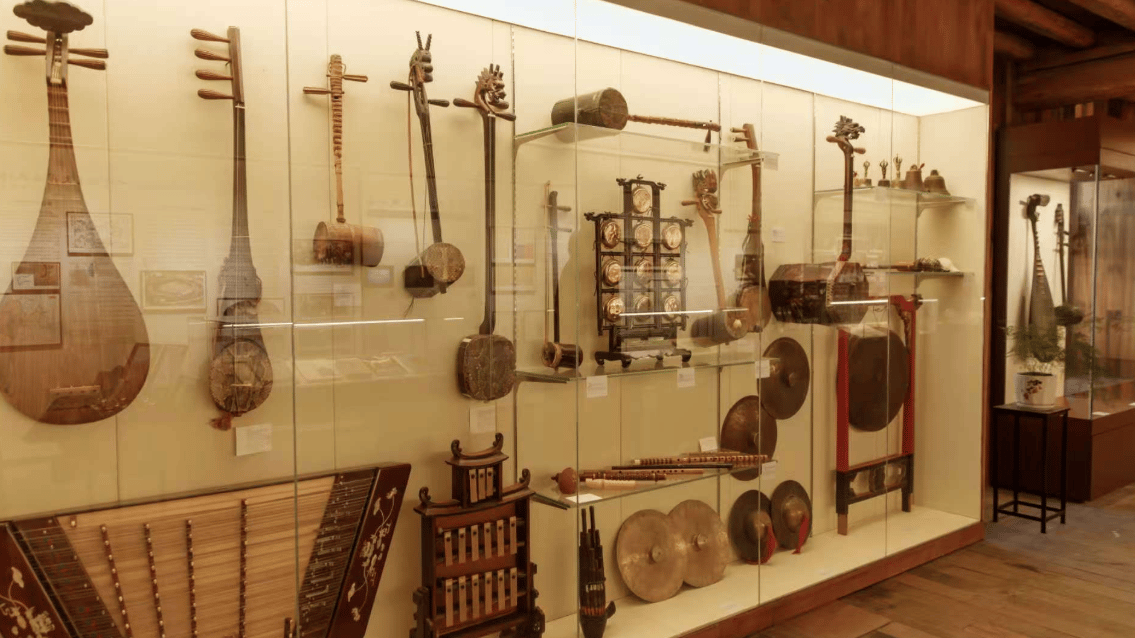 Collection of traditional Chinese musical instruments like the pipa, erhu, and gongs in a museum display case.