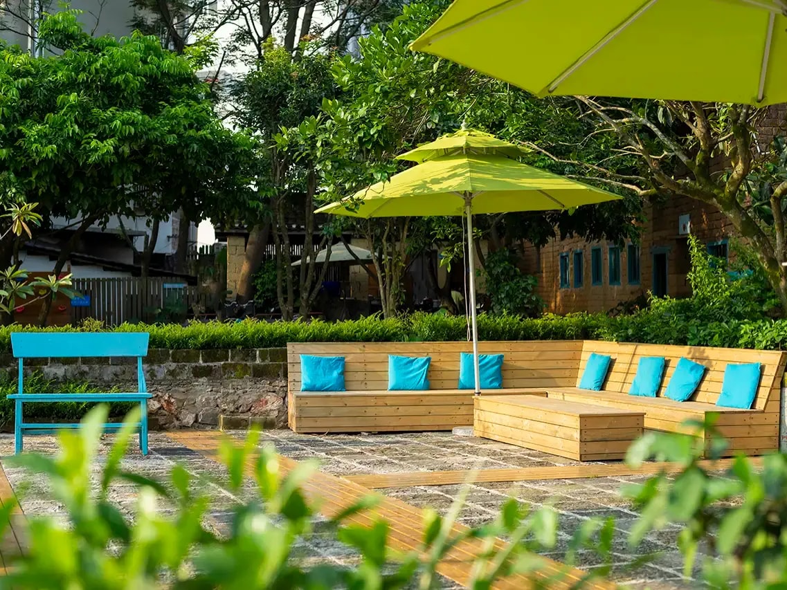 Wooden bench seating with turquoise cushions under lime parasols, mud-brick farmhouse behind
