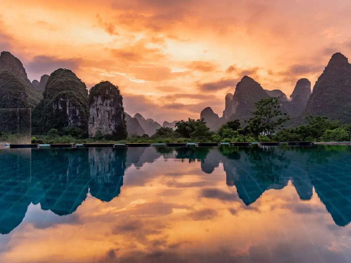 Still pool at sunset mirroring an orange sky and a row of karst peaks