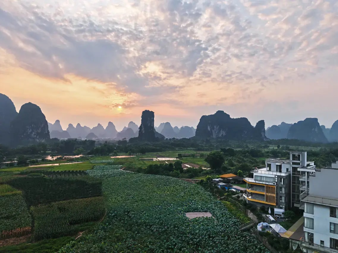Modern hotel block above lotus fields at sunrise with karst peaks on the horizon