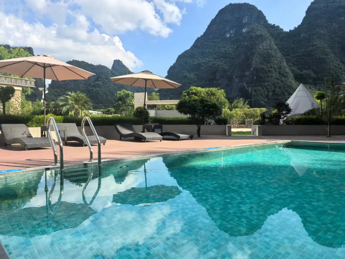 Turquoise pool with cream parasols and loungers, karst peaks rising behind the hedge