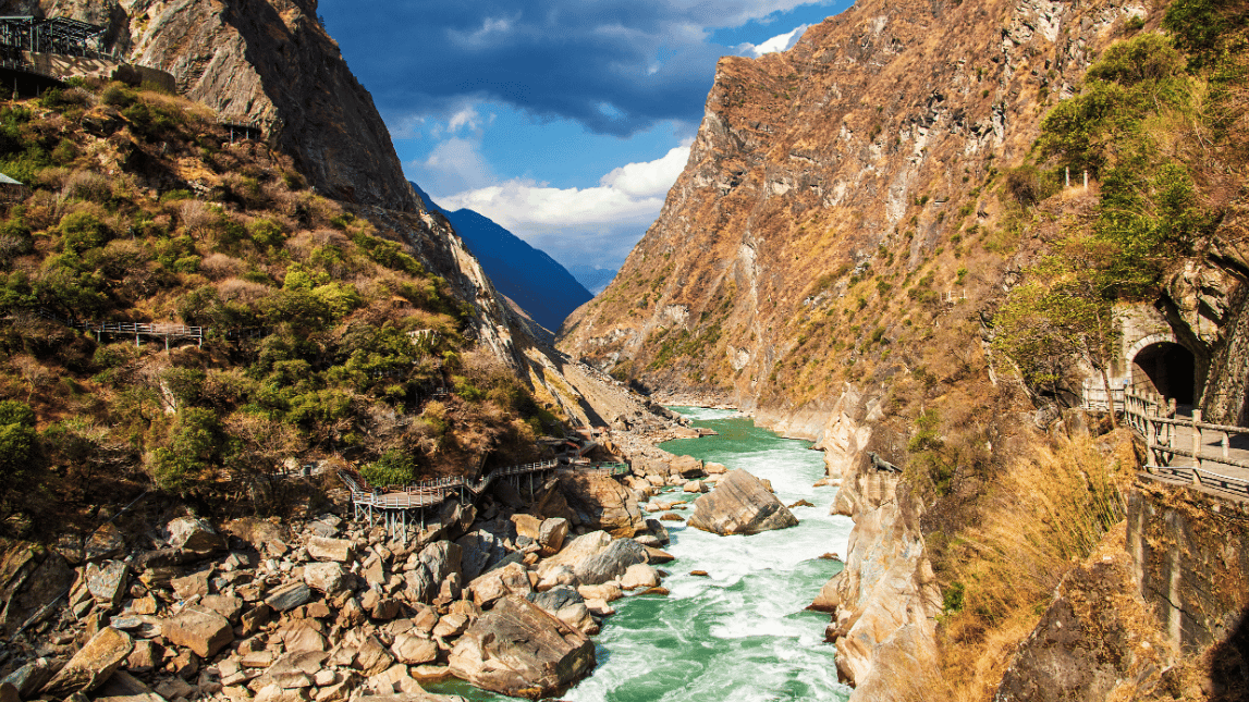 A scenic view of Tiger Leaping Gorge with the Jinsha River flowing between steep canyon cliffs in Yunnan, China.