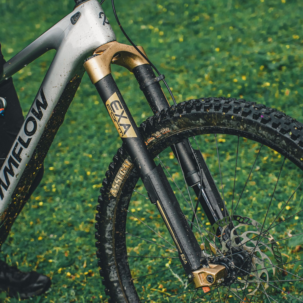 Mud-splashed silver Amflow e-MTB frame and front suspension fork on green grass