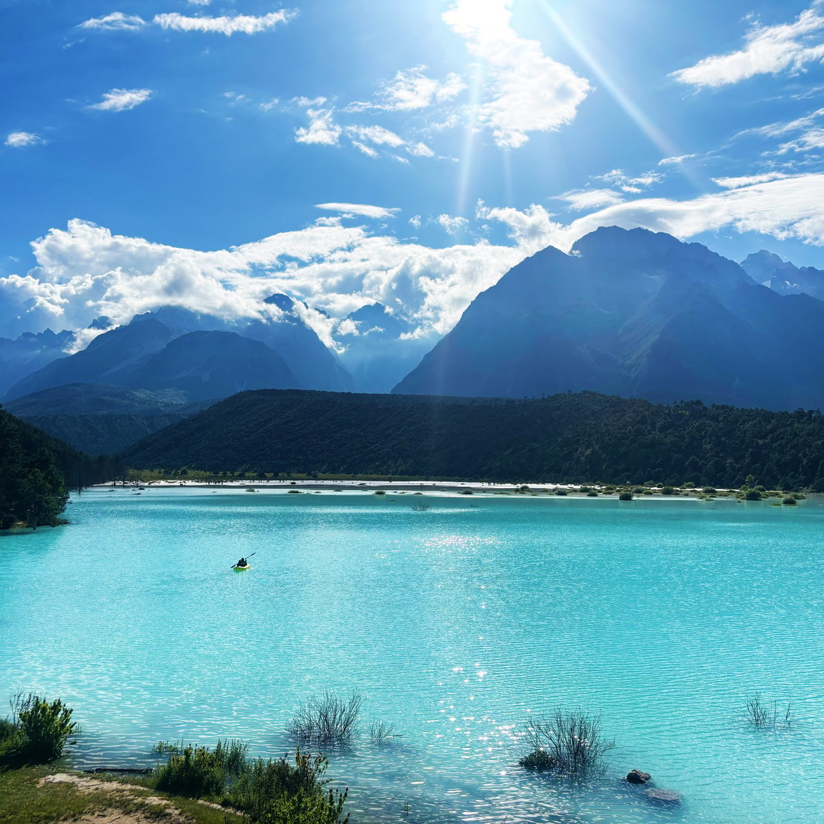 Kayaker on a turquoise lake with white shores, Jade Dragon Snow Mountain under bright sun and cloud