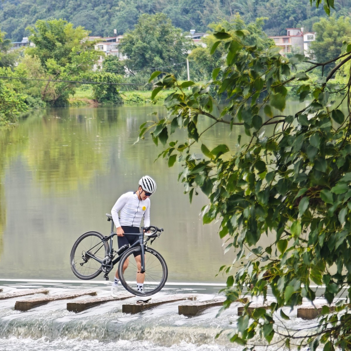 Rider carrying a bike across a low weir with water spilling over the lip