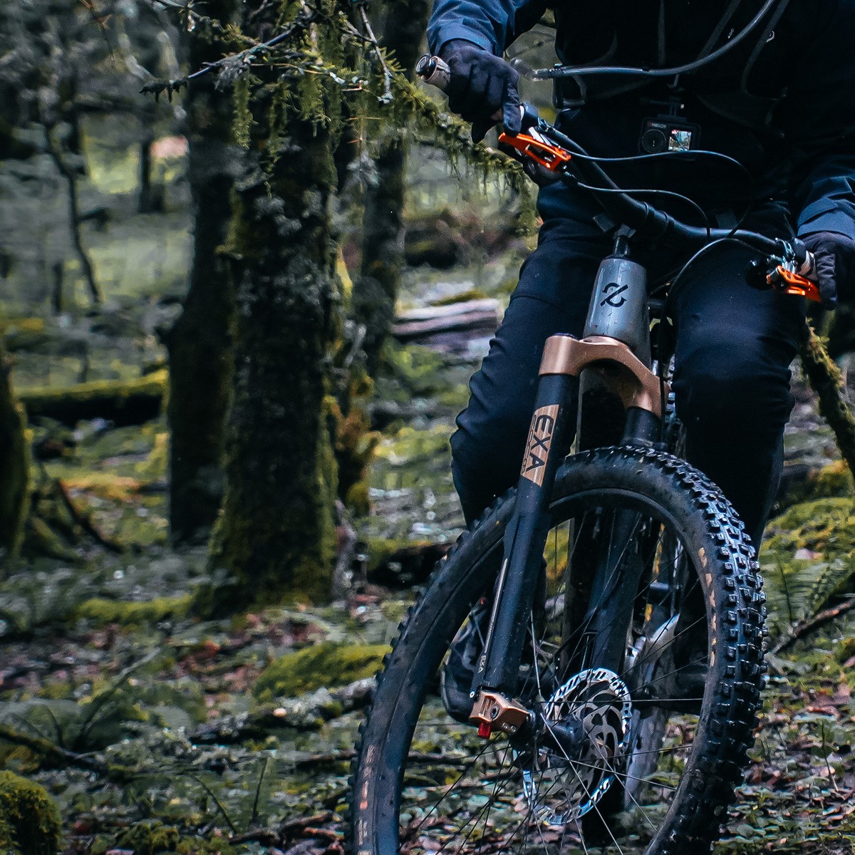 Close-up of a rider on an Amflow e-MTB with a gold suspension fork on a mossy forest trail