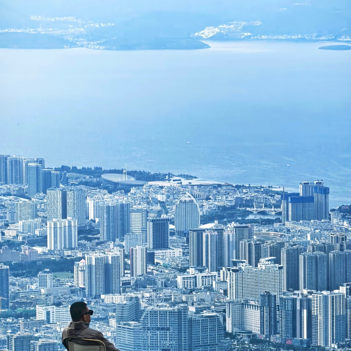 Rider resting in a camp chair on the ridge, looking down over Dali city and Erhai Lake