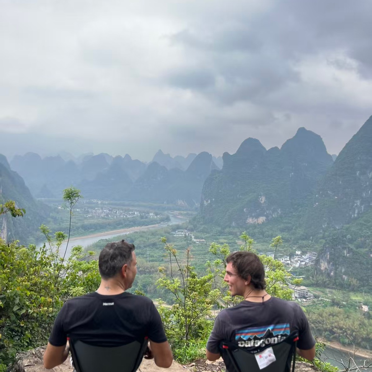 Two riders resting on camp chairs at a clifftop viewpoint over the river valley