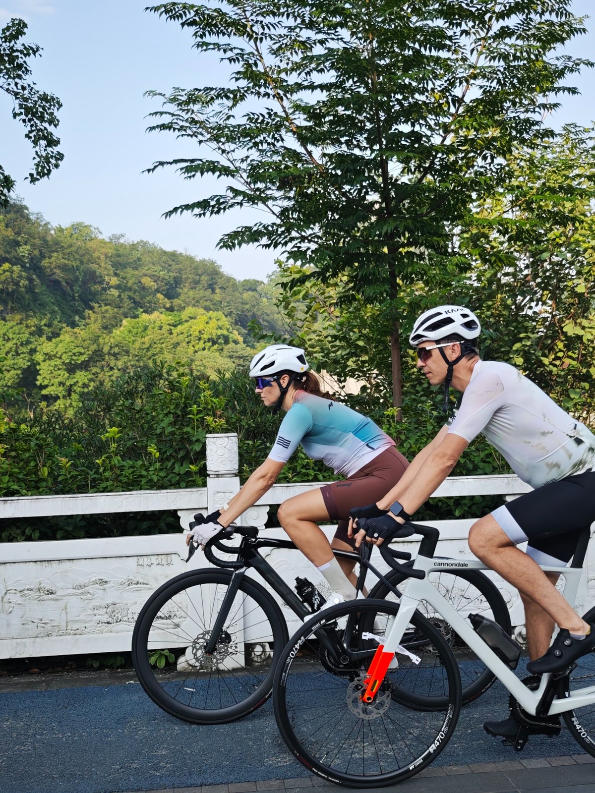 Two riders passing a carved white stone balustrade on a bridge