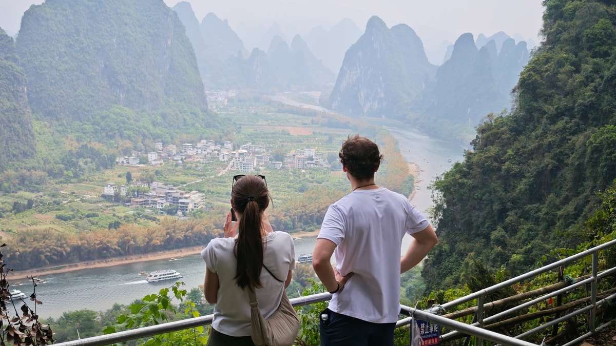 Two guests at a railed viewing platform above the river, a cruise boat passing below