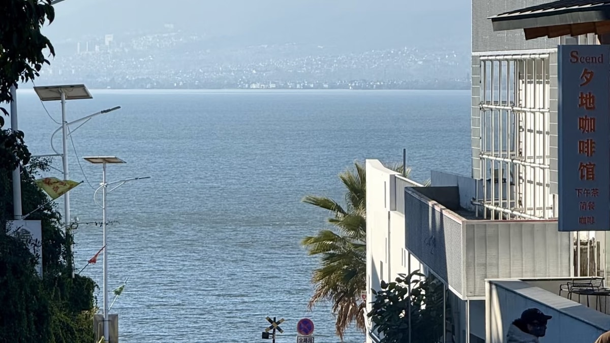 Village street sloping down to Erhai between white buildings, mountains across the water