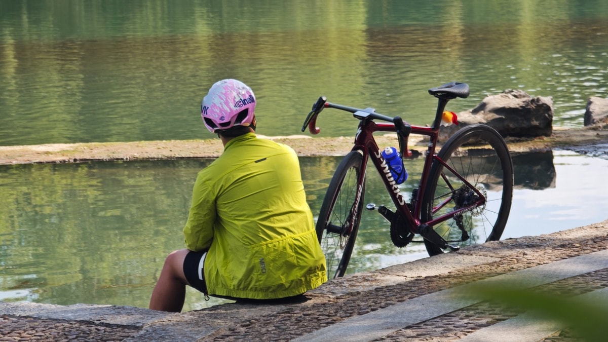 Rider sitting on the stone bank beside the bike, the river still and green