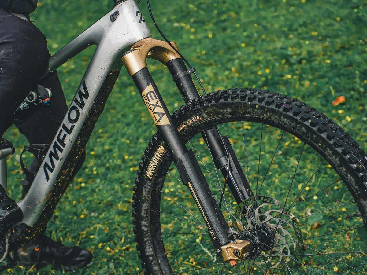 Mud-splashed silver Amflow e-MTB frame and front suspension fork on green grass