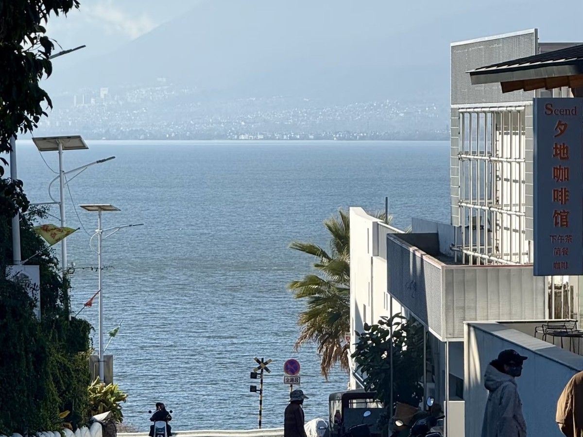 Village street sloping down to Erhai between white buildings, mountains across the water