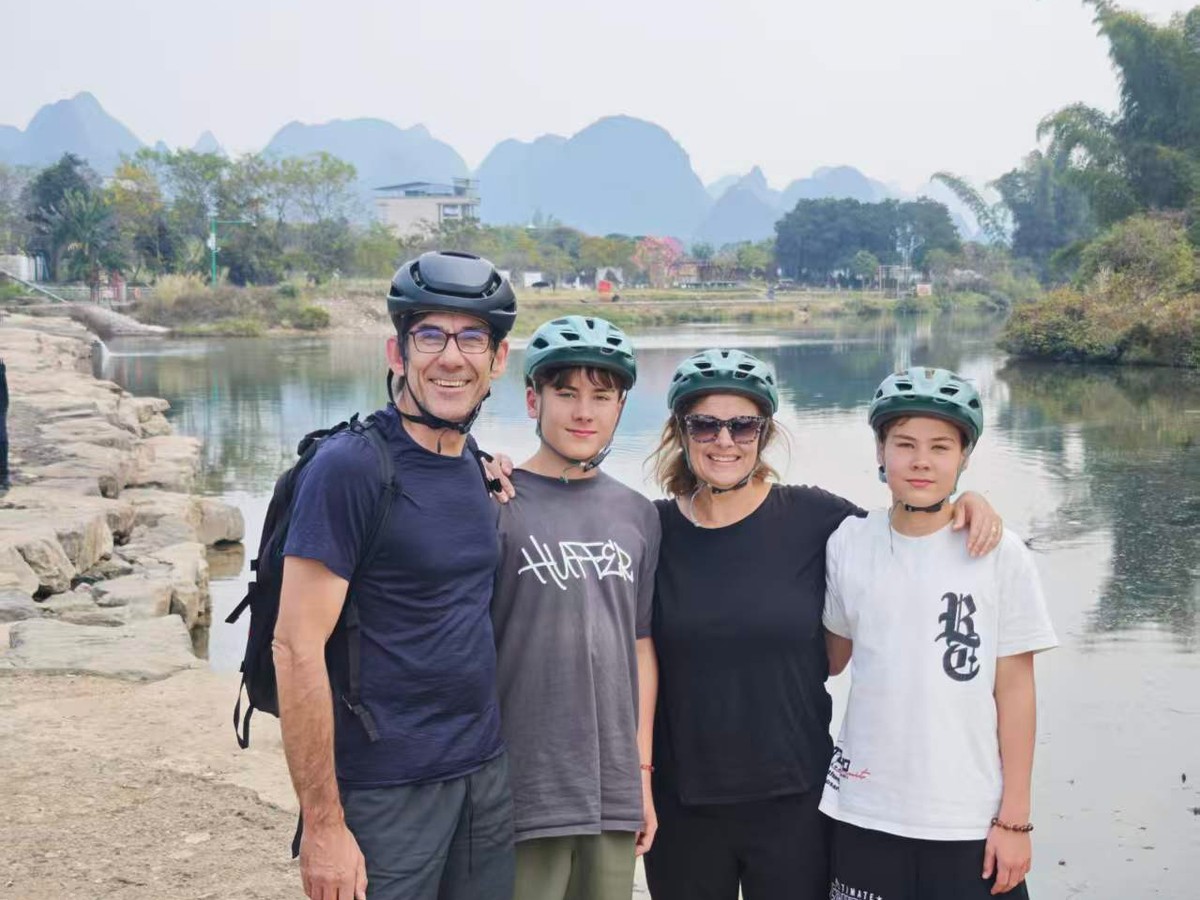 Family of four in helmets on the riverbank with karst peaks behind