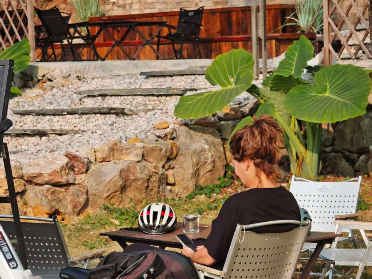 Guest with coffee at an outdoor cafe table, helmet on the table and bikes parked alongside