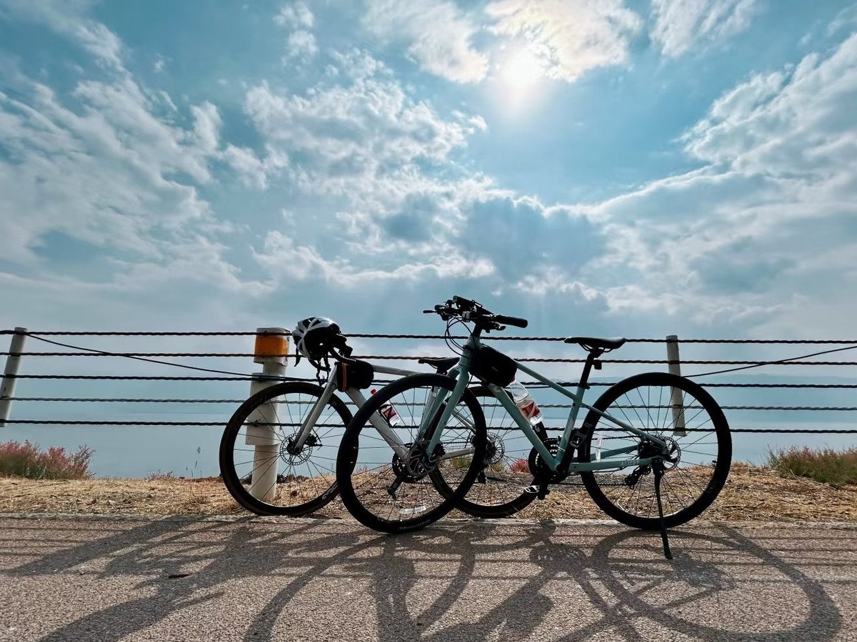 Two bikes parked against a rope railing on the lakeside path under a bright sky