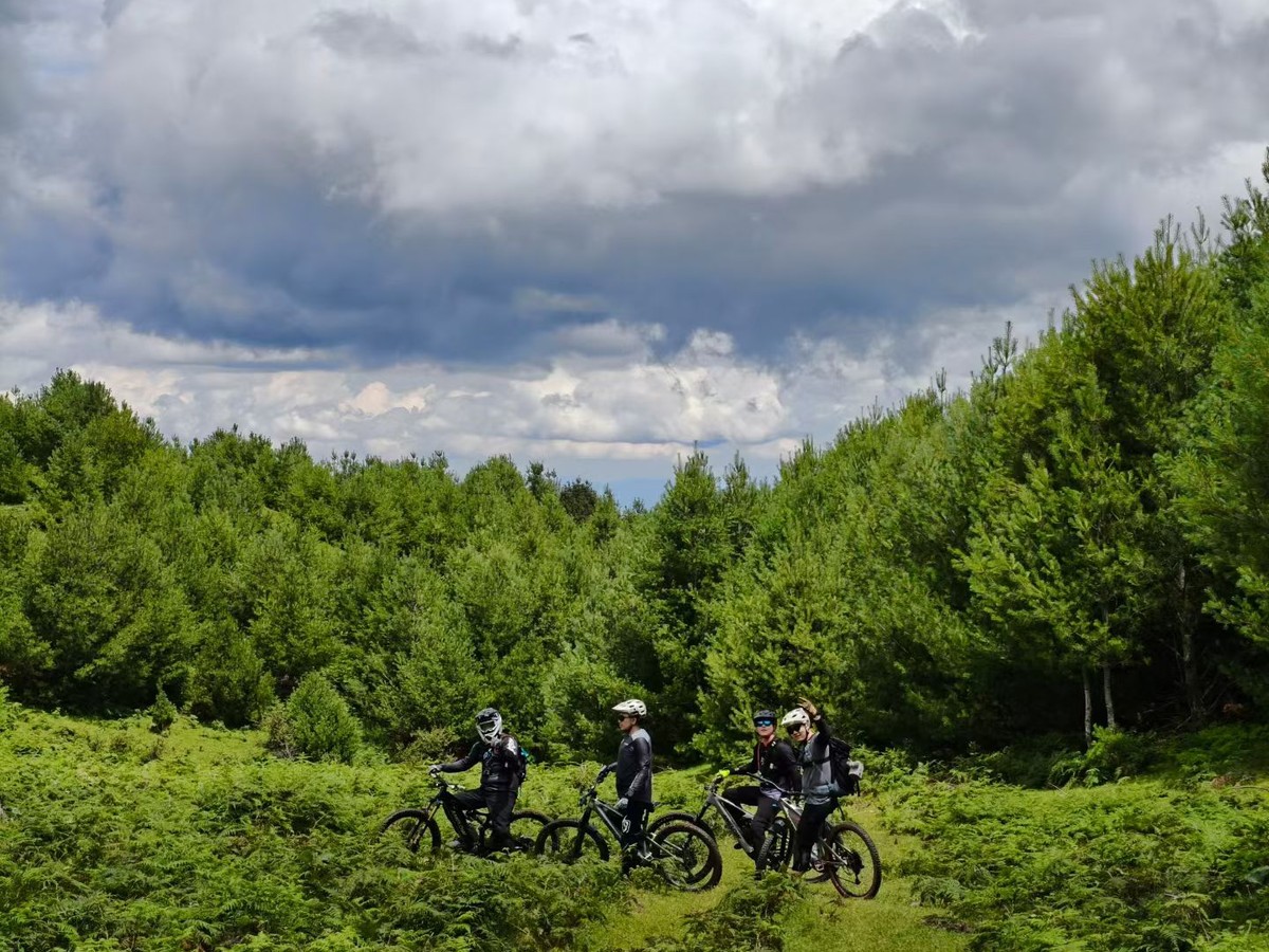 Three riders with e-MTBs in a green mountain meadow under big clouds