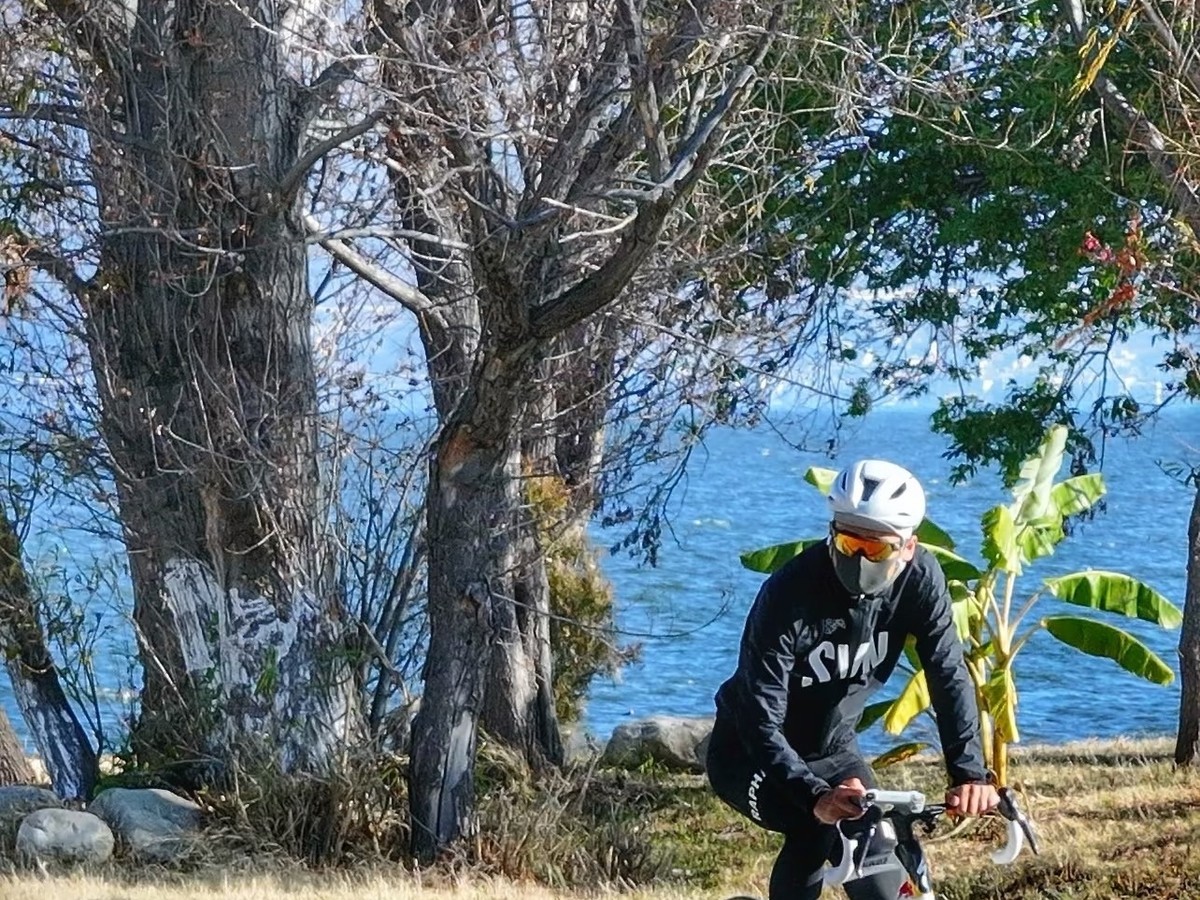 Cyclist riding along the lakeside path under bare trees beside the water