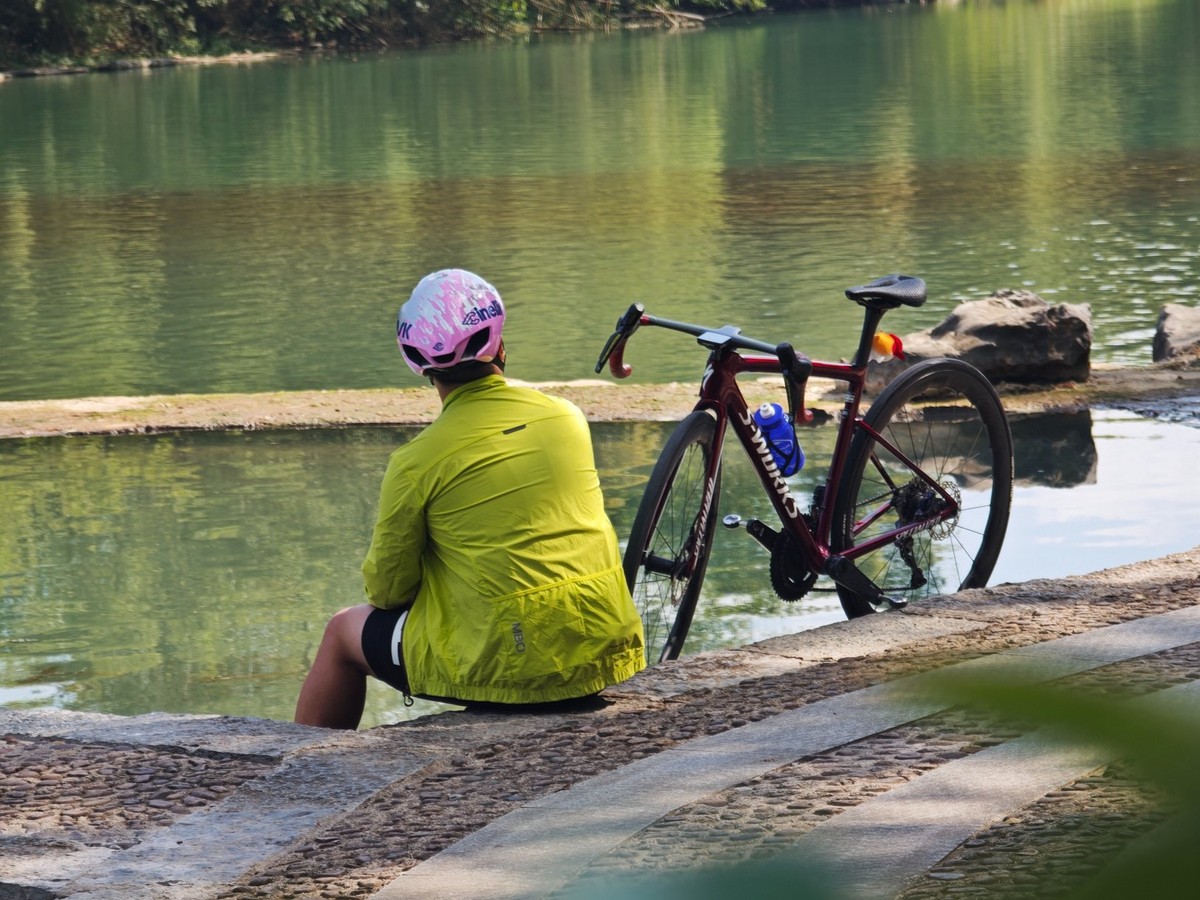 Rider sitting on the stone bank beside the bike, the river still and green