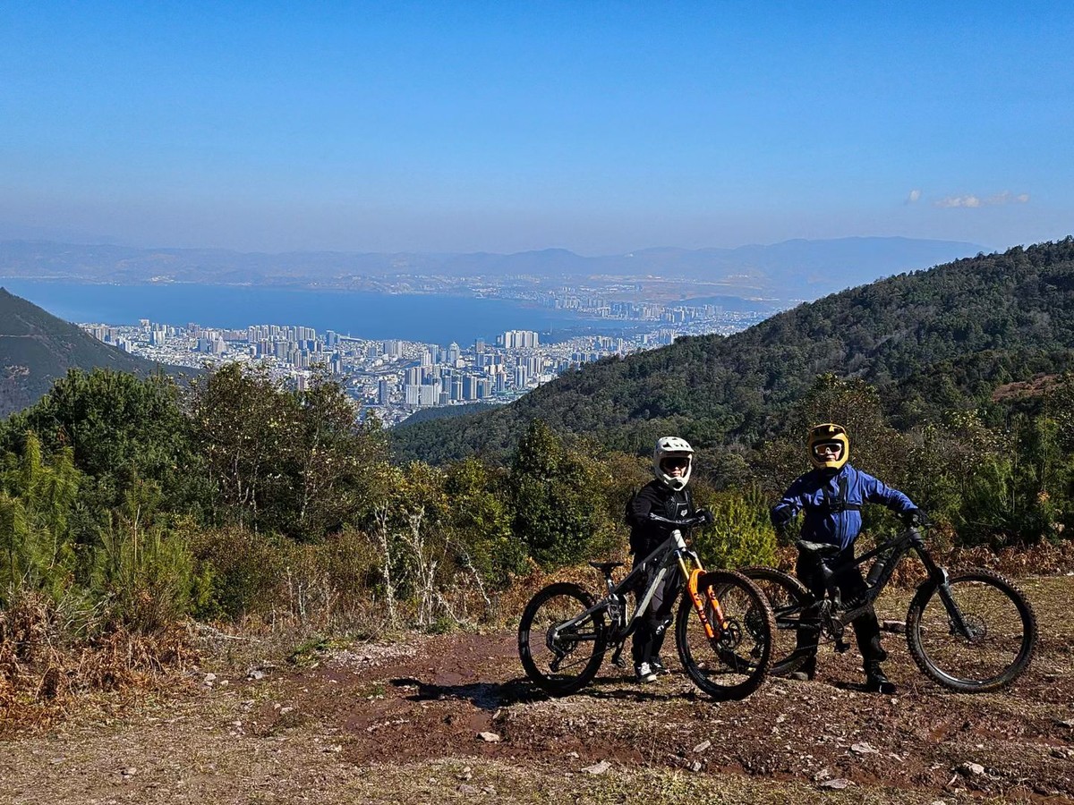 Two riders in full-face helmets with their e-MTBs on a ridge above Dali and Erhai Lake