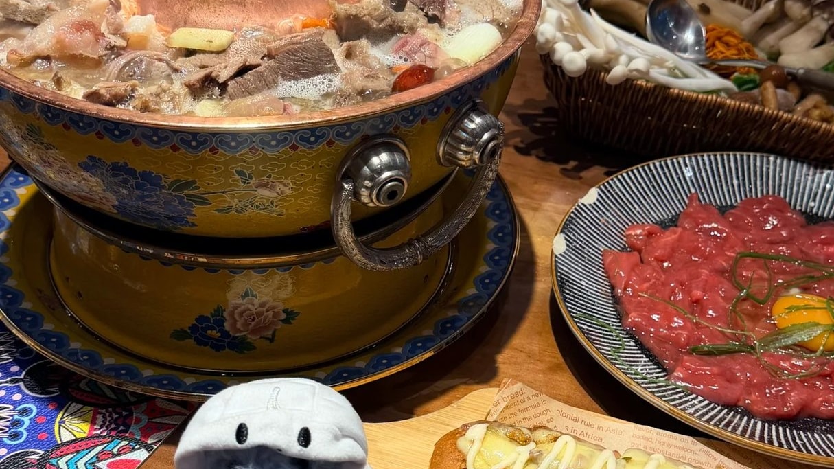 A copper chimney hotpot of yak meat simmering on a table set with side dishes.