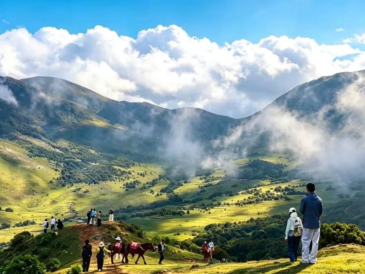 Visitors and horses on a grassy ridge on Niaodiao Mountain, with cloud drifting through the green valleys below