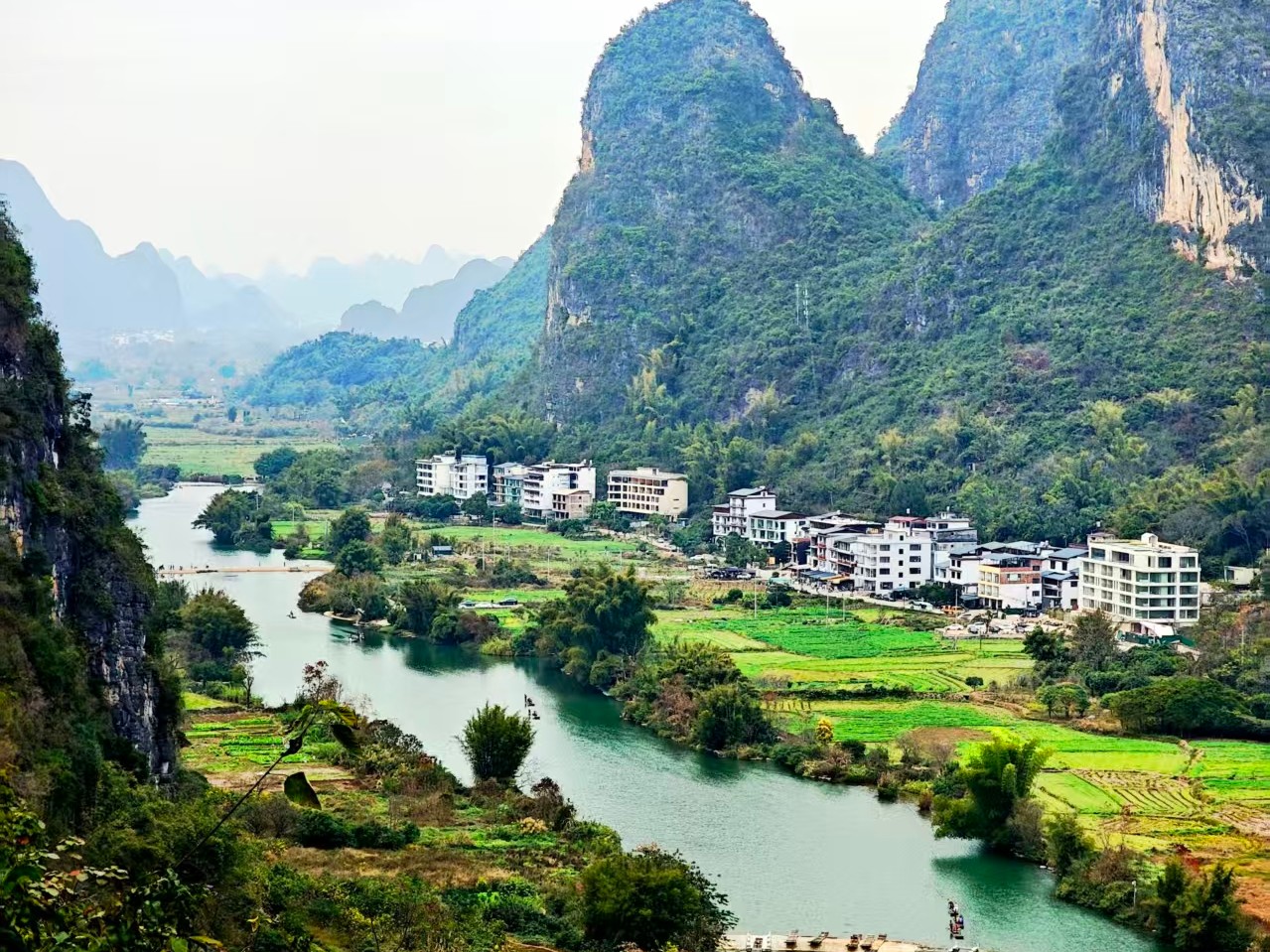 Green river below overhanging trees with a village and hills on the far bank