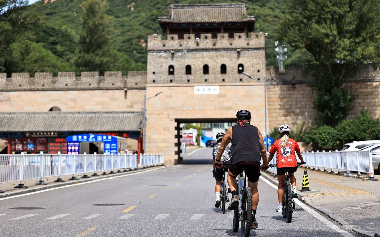Cyclists riding toward a stone gate tower with crenellated walls on a road outside central Beijing