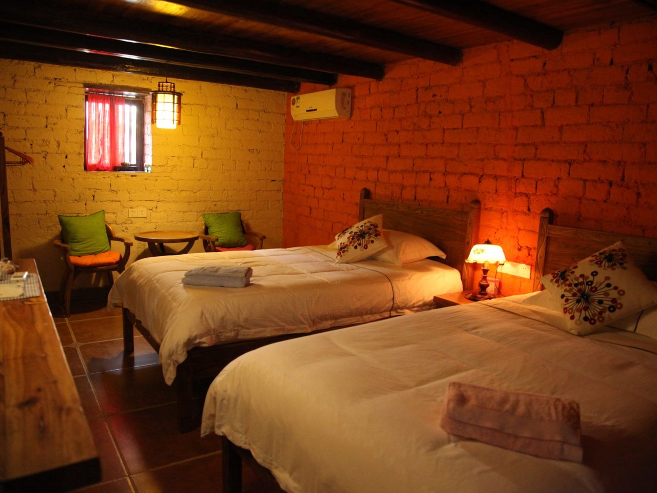 Twin beds under timber beams in a room with painted mud-brick walls and a lamp lit warm