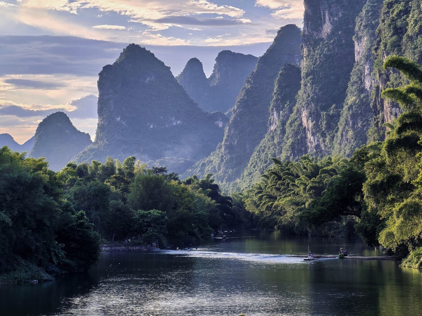 Two punted bamboo rafts on calm water below sunlit karst peaks