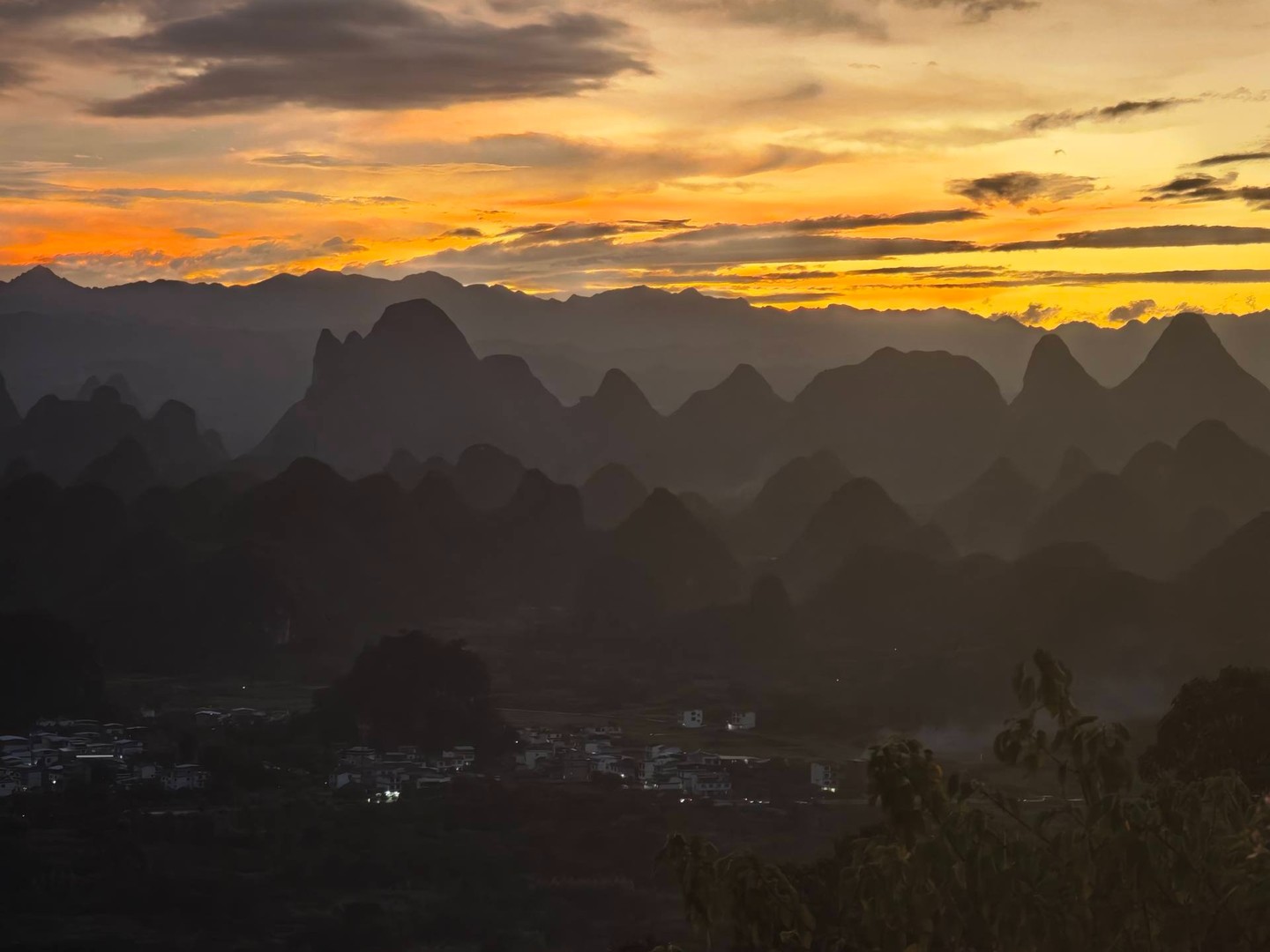 Sunset over layered karst ridges with a village lit in the valley below