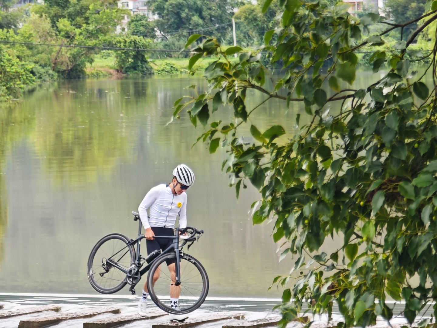 Rider carrying a bike across a low weir with water spilling over the lip