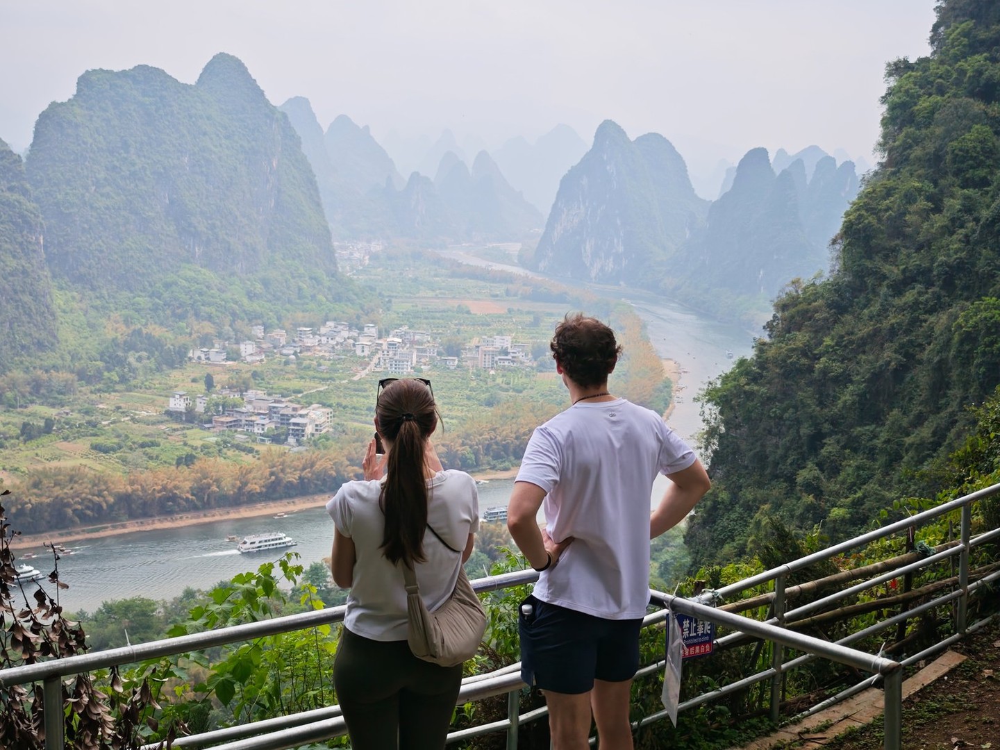 Two visitors at a railed viewing platform above the river, a cruise boat passing below
