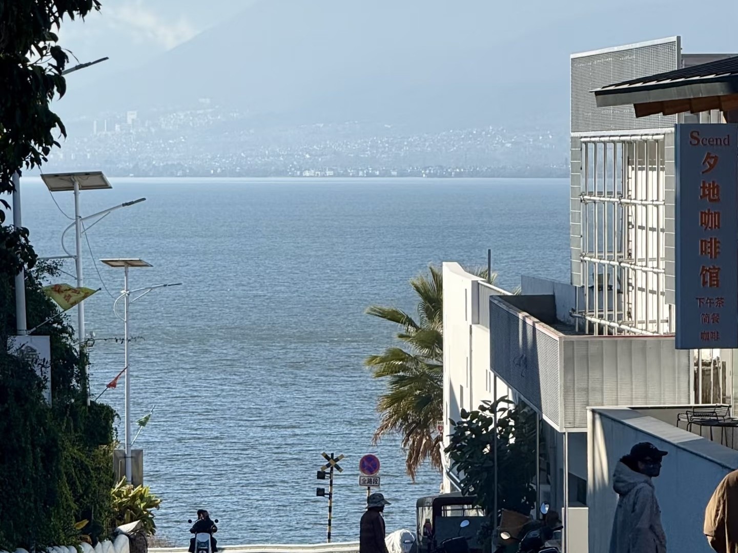 Village street sloping down to Erhai between white buildings, mountains across the water