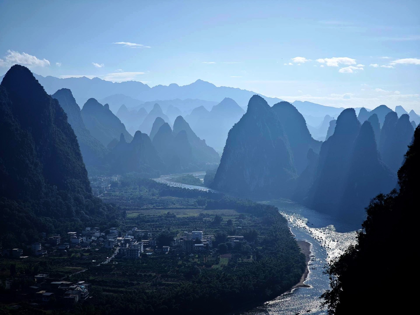 Hazy karst peaks above a bend of the Li River with a riverside village below