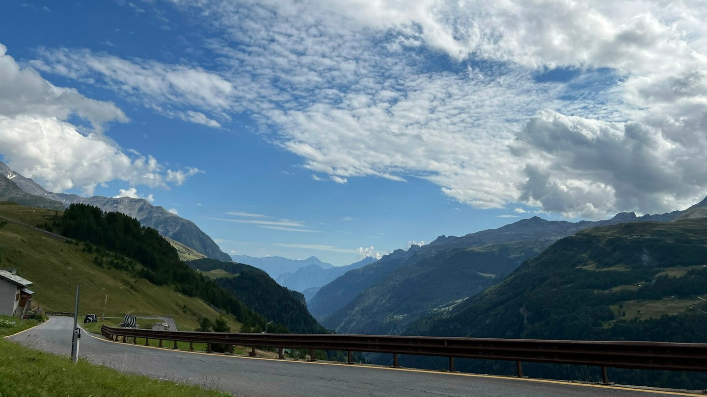 A winding mountain road curving above a wide valley.