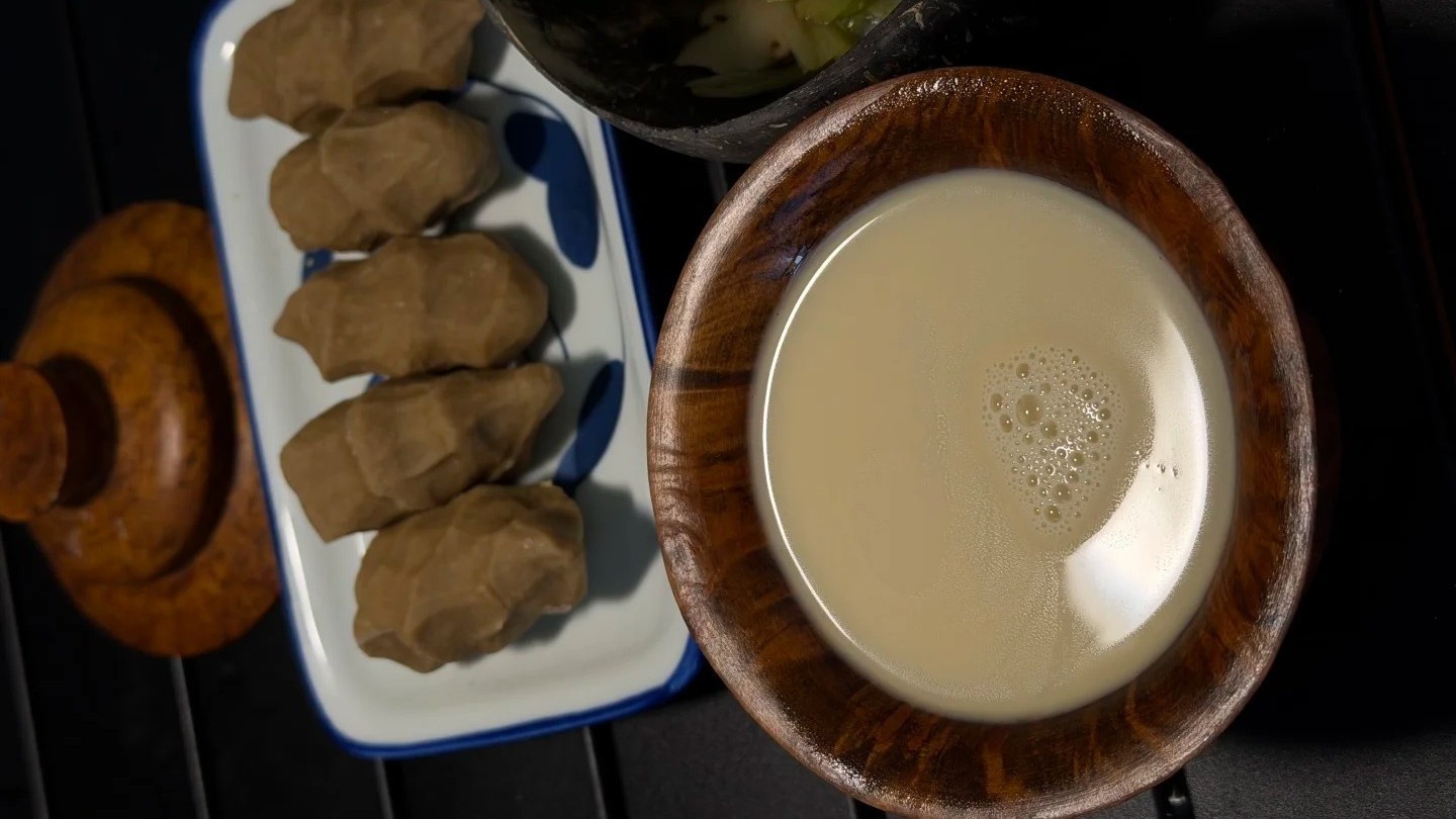 Pieces of tsampa on a dish beside a wooden bowl of freshly poured butter tea.