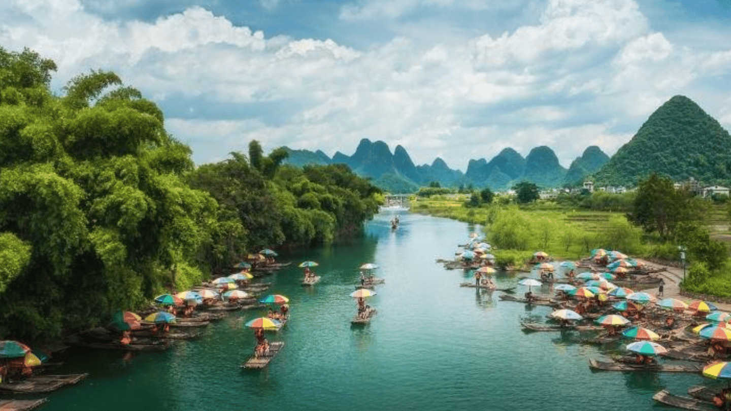 Traditional bamboo rafts with colorful umbrellas on the Yulong River in Yangshuo, China, with karst mountains.