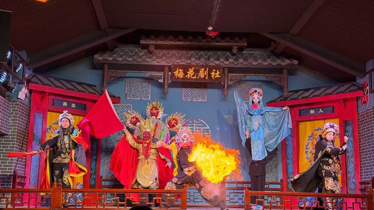 Sichuan Opera performers in painted masks and a fire-spitting act on a red and gold stage.