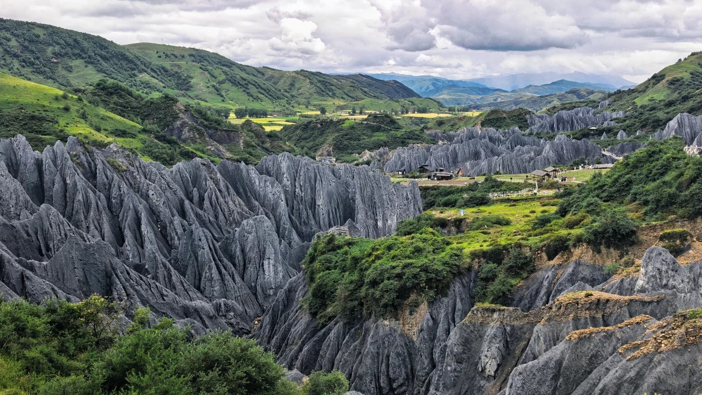 Grey slate pillars of the Bamei Black Stone Forest rising from a green valley floor.