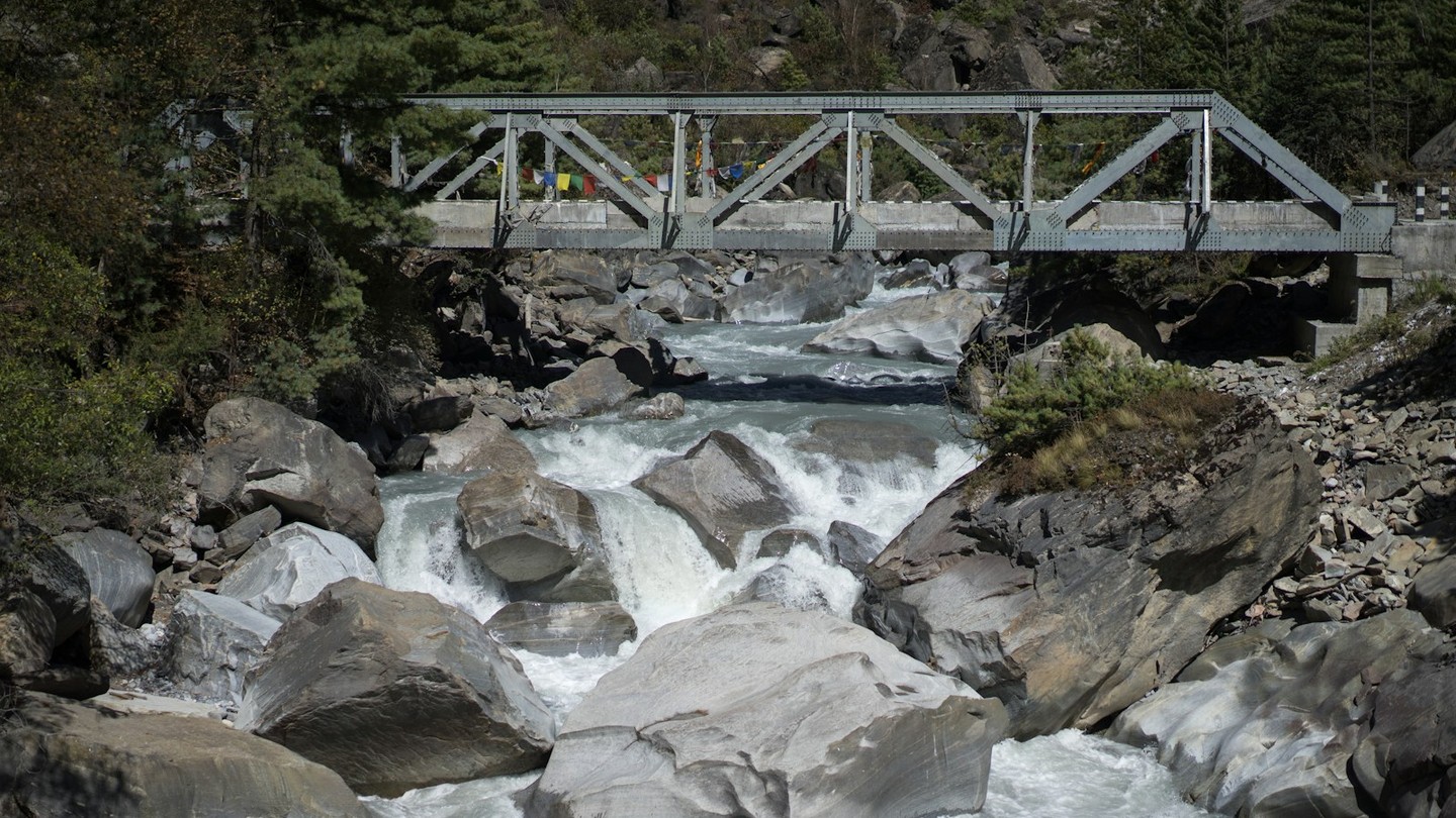 A grey metal bridge spanning a clear mountain river.